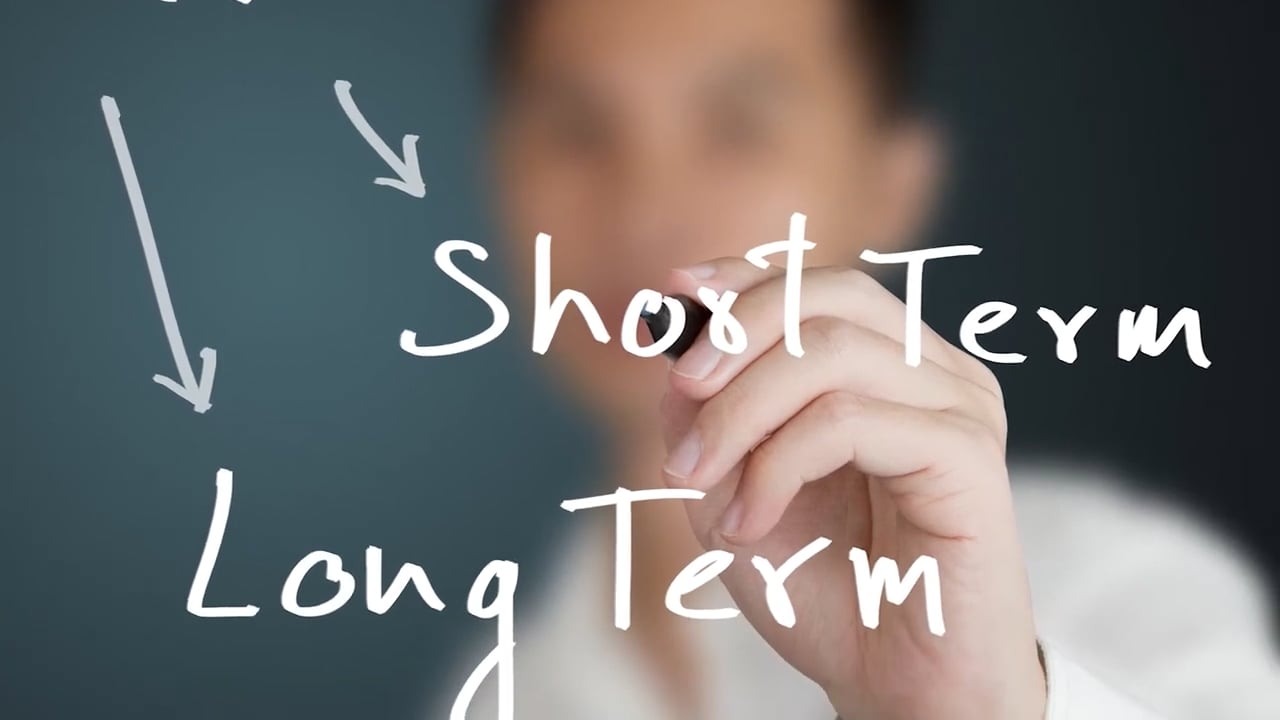 A man writing on glass with a marker with arrows pointing to short term and long term.